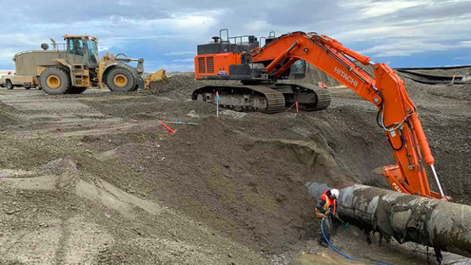 Excavator digs hole around pipe